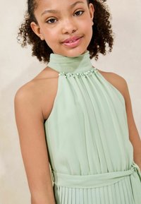 Robe plissée vert clair avec un col montant, ornée de perles au col. Dispose d'une taille à lien, fabriquée à partir d'un tissu lisse et fluide.