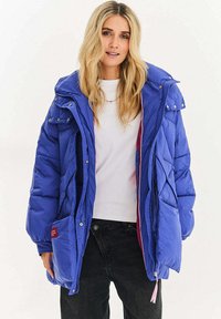 Prošívaná modrá bunda s kapucí, vybavená předním zipem, bočními kapsami a kontrastní růžovou podšívkou. Texturovaný materiál.