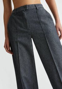 Ciemnoniebieskie spodnie o szerokich nogawkach z wyraźnymi zmarszczkami, dopasowanym paskiem w talii oraz kontrastowymi białymi stębnowaniami. Materiał jest gładki w dotyku.