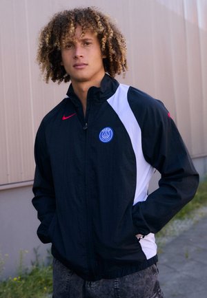 Black and white windbreaker jacket with a full-zip design, featuring a blue logo and red accents on the collar and left shoulder.
