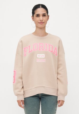 Béžena majica s kapuco z napisom "FLORIDA" in "MIAMI" v rožnati pisavi. Ima rebraste manšete, spuščena ramena in sproščen kroj.