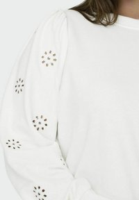 Felpa bianca con maniche a sbuffo e ricami floreali in pizzo. Tessuto morbido, design minimalista e dettagli delle maniche a polsino.