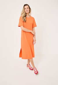 Rochie scurtă cu mânecă scurtă de culoare portocalie, cu o fanta laterală, fabricată dintr-un material moale. Asortată cu adidași multicolori, cu accente roz și albe.