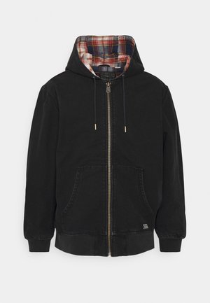 Zwarte capuchonjas met ritssluiting, voorzakken, trekkoorden en een voering van geruite stof aan de binnenkant van de capuchon.