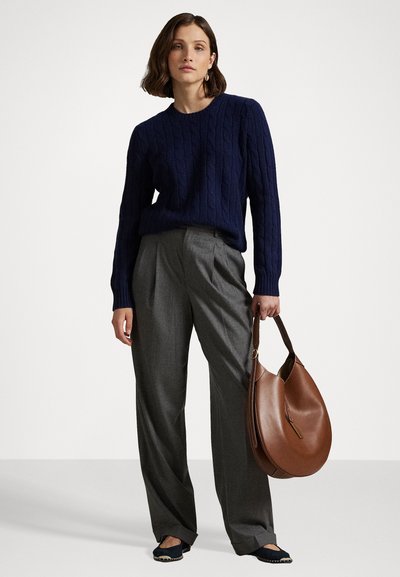 Marineblaue Kabelstrickpullover, hochgeschnittene graue Hose und braune Hobo-Tasche. Das Model trägt schwarze Slipper mit weißen Steppakzenten.