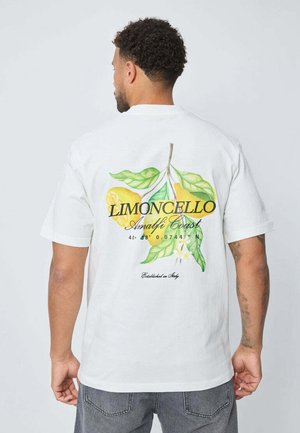 T-shirt en coton blanc avec un imprimé coloré de citrons et de feuilles, accompagné du texte "LIMONCELLO Côte Amalfitaine" et des coordonnées géographiques.