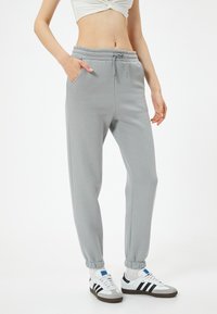 Lichtgrijze sweatpants met een elastische tailleband, zijzakken en elastische boorden. Gecombineerd met witte sneakers met zwarte strepen.