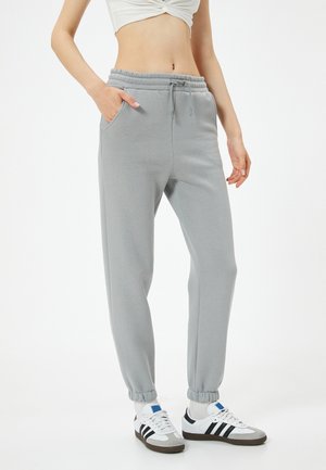 Light gray sweatpants with an elastic waistband, side pockets, and elastic cuffs. Paired with white sneakers featuring black stripes.
