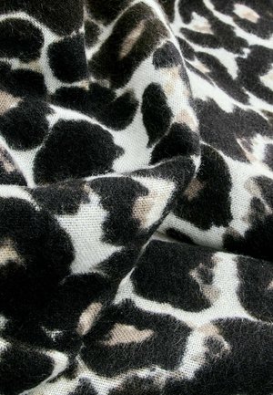 Schwarzer und beiger Tierdruckstoff mit einer weichen, flauschigen Textur, der unregelmäßige Flecken auf weißem Hintergrund zeigt.