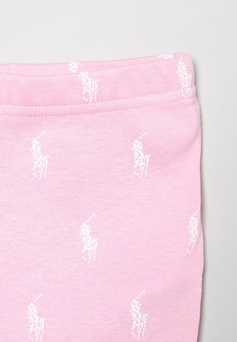 Jasnoróżowa tkanina o miękkiej fakturze, z powtarzającymi się małymi białymi logotypami graczy polo. Elastyczny pas u góry.