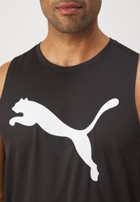 Zwart mouwloos sportshirt met een groot wit Puma-logo op de voorkant, gemaakt van gladde, lichte stof.