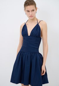 Robe halter bleu marine avec un décolleté en V profond, un corsage froncé et une jupe évasée. Fabriquée en tissu texturé avec des bretelles réglables.