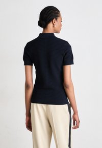Polo navy a maniche corte con un design a coste testurizzato. Presenta un colletto classico e una silhouette aderente. Indossato con pantaloni beige.