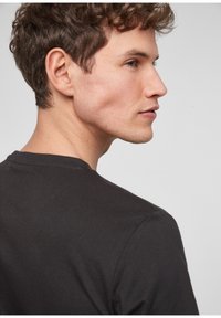 Zwarte katoenen t-shirt met een ronde hals, korte mouwen en een gladde textuur, zijwaarts weergegeven om de pasvorm te tonen.