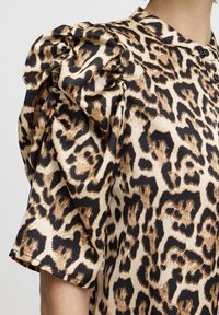 Blouse imprimée léopard avec des manches courtes bouffantes, des boutons noirs et une texture lisse semblable à du satin dans des nuances de brun, beige et noir.