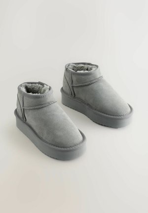 Grå mocka ankelstövlar med foder av shearling, rundad tå och platt gummisula. Utrustad med ett omlottband för en snug passform.