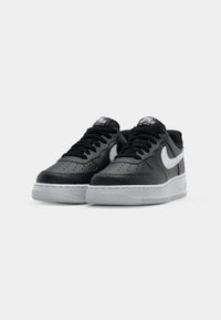 Crne kožne tenisice s teksturiranom površinom, s bijelim Nike swooshom, crnim vezicama i sivom gumenenom potplatom. Dizajn s perforiranim vrhom.