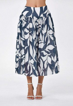Jupe midi fluide taille haute avec motif abstrait de feuilles blanches sur fond bleu marine, portée avec des talons blancs à bride de cheville.