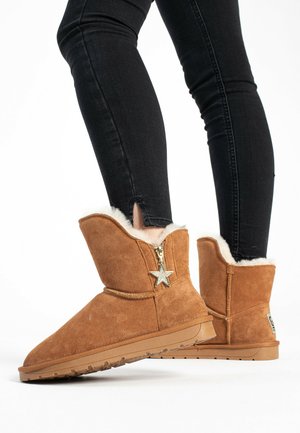 Tan suede ankle boots with a fur lining and a gold star zipper pull. The sole is textured for grip, and the upper features a fold-over design.