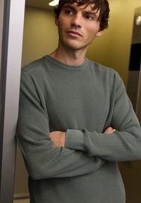 Pull gris à manches longues en maille gaufrée avec un col et des poignets côtelés, présentant un motif texturé et une coupe décontractée.