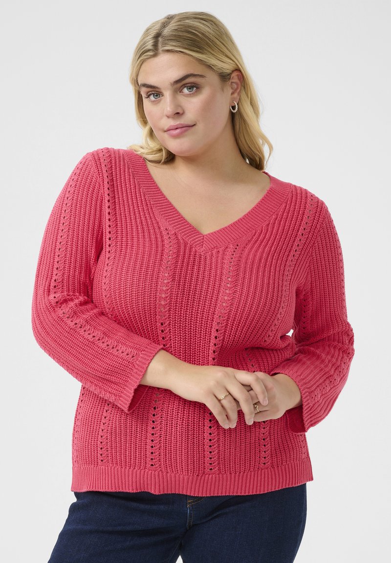 Pull en tricot rose avec décolleté en V, présentant un tissu texturé, des motifs complexes de couture ouverte et des manches trois-quarts.