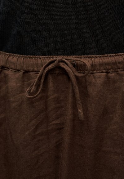 Καφέ λινή φούστα με ελαστική μέση και λεπτομέρεια κορδονιού δεμένης. Το ύφασμα έχει υφή με διακριτικές ρυτίδες.