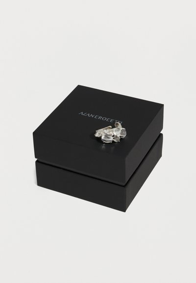 Μαύρο κουτί κοσμημάτων με ασημένιο κείμενο λογότυπου, με ένα ζευγάρι ασημένια σκουλαρίκια με πολλούς διάφανους πολύτιμους λίθους στην κορυφή.