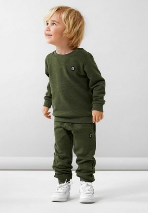 Ensemble en coton vert composé d'un sweat-shirt et d'un pantalon de jogging avec un petit logo noir, associé à des baskets blanches, comportant des poignets côtelés et une taille élastique.