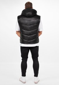 Zwarte leren puffer vest met een hoge kraag, met een doorgestikt ontwerp en een soepele textuur, gedragen over een wit shirt en zwarte jeans.