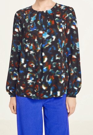 Langærmet bluse med abstrakt mønster i sort, blå, rød og hvid, kombineret med lyseblå bukser.