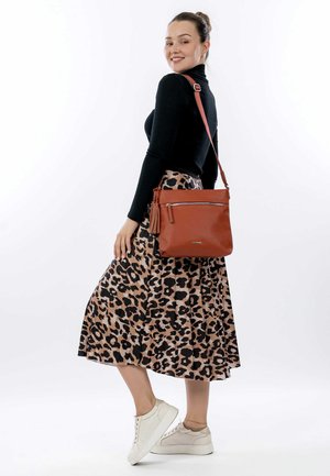 Brown leather crossbody bag with a zippered front pocket and tassel detail. Worn with a black turtleneck and a leopard-print midi skirt.