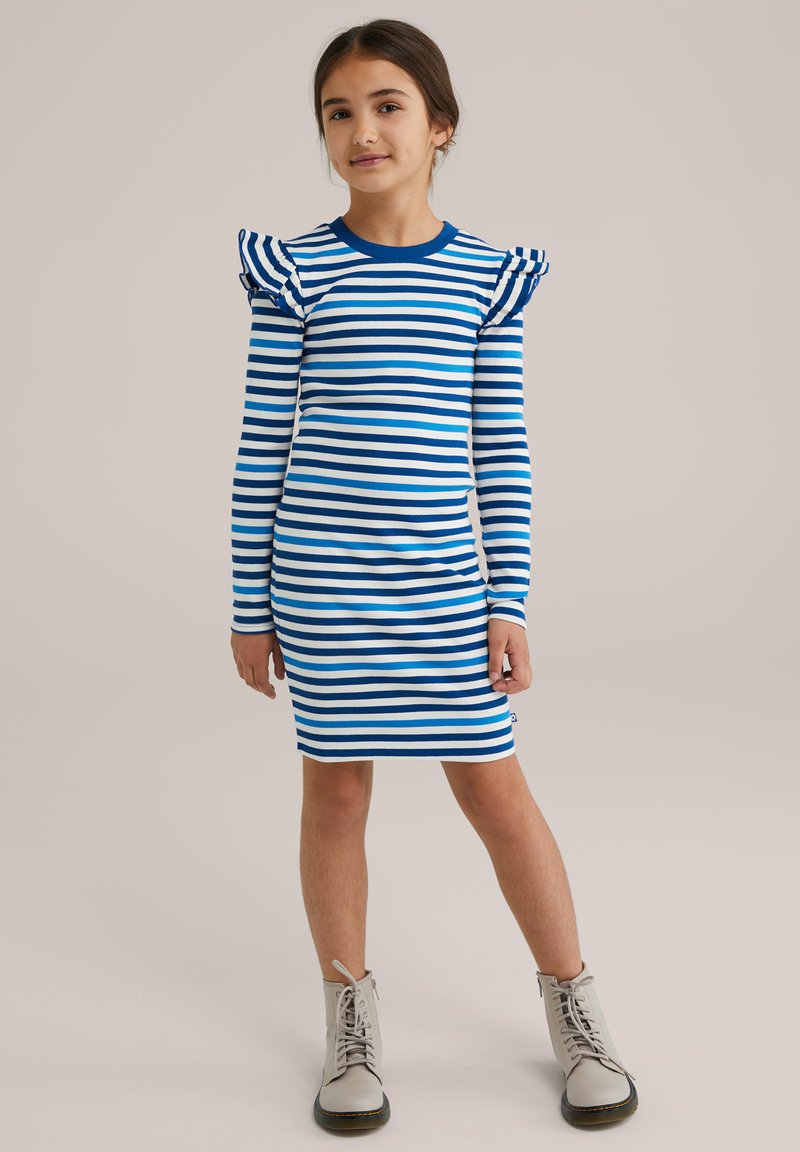 Gestreiftes Kleid mit blauen und weißen horizontalen Streifen, langen Ärmeln, gewellten Schulterakzenten und körperbetontem Design, kombiniert mit hellgrauen Stiefeln.