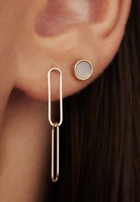 Goldfarbene Ohrringe mit einem geometrischen, länglichen Ovaldesign und einem kleineren, runden Akzentstein, beide am Ohrläppchen befestigt.