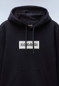 Black hoodie with a large white rectangular graphic label featuring "NAPAPIJRI geographic." Soft material, drawstrings, and front pocket.
