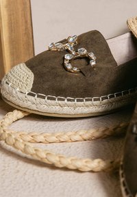 Espadrilles in suede marrone con suola in juta intrecciata, caratterizzate da un accento decorativo di strass e un design a punta chiusa e arrotondata.