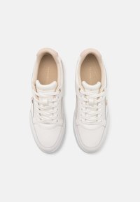 Zapatillas de cuero blancas con una textura suave, puntera redonda y acentos tonales. Presentan un cierre con cordones y detalles del logo en dorado en el costado.