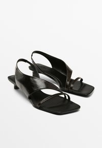 Schwarze Leder-Sandalen mit einem niedrigen Blockabsatz, offenem Design und überkreuzten Riemen im Obermaterial, mit quadratischer Zehenform.
