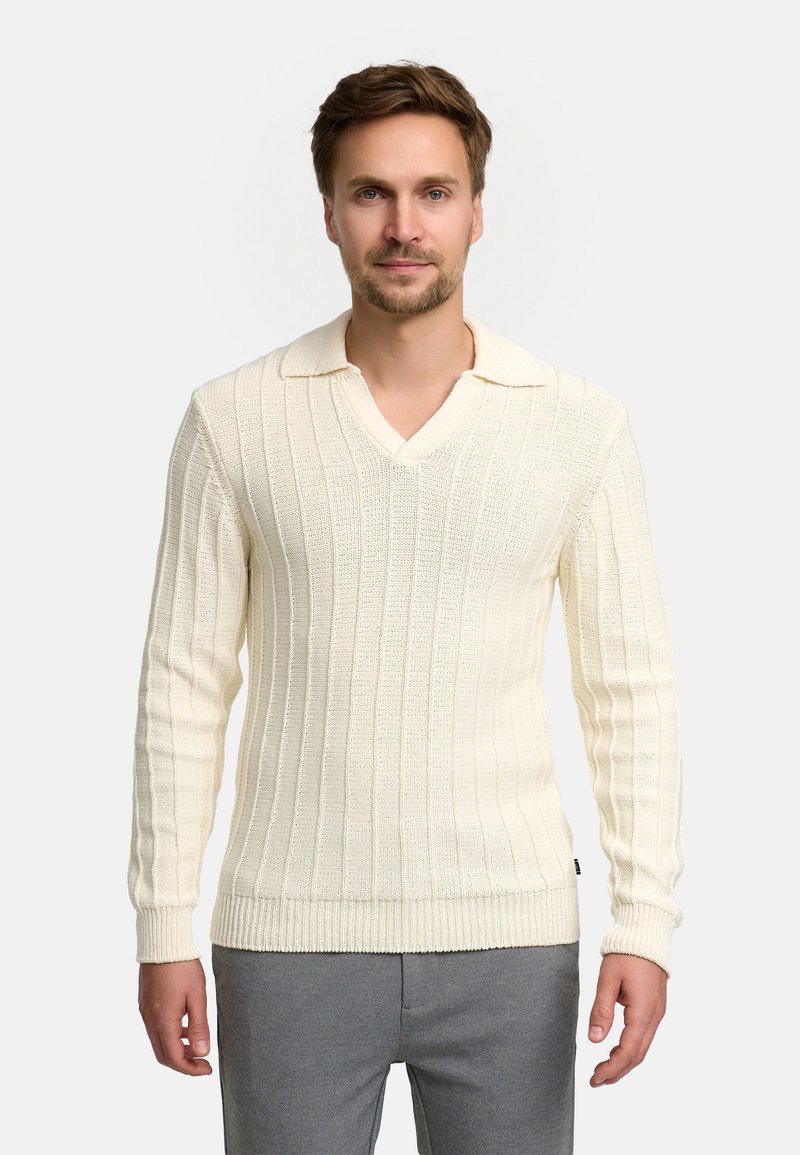 Maglione a maglia color crema con scollo a V, texture a coste verticali, maniche lunghe e colletto ripiegato. Indossato con pantaloni grigi.