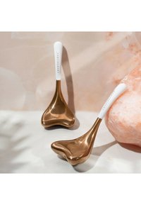 Dwa ergonomiczne łyżki z błyszczącymi złotymi metalowymi końcówkami i białymi uchwytami, z napisem "CRYSTALLOVE". Gładki, nowoczesny design.