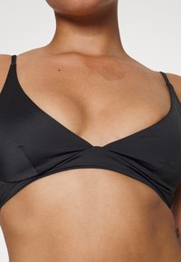 Top de biquíni preto com decote em V, alças finas ajustáveis e um design cruzado no centro. Textura de tecido suave e elástico.