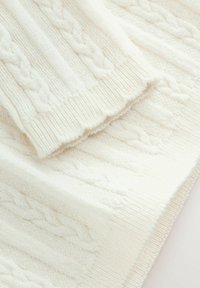 Tissu en tricot crème présentant un motif en torsade avec des bords côtelés ; texture douce et épaisse avec des détails raffinés sur toute la surface du tissu.
