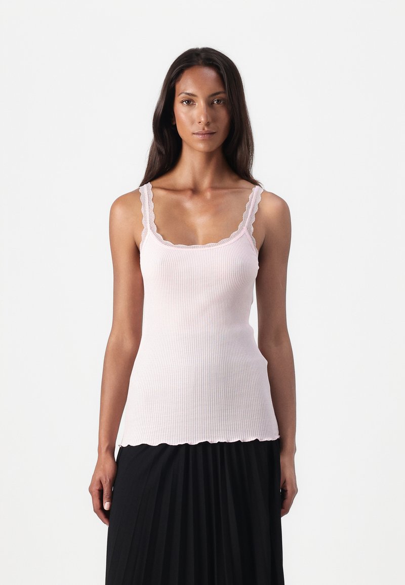 Top aderente rosa pallido a coste con spalline e orlo ondulati, caratterizzato da un design fitted e una texture morbida.