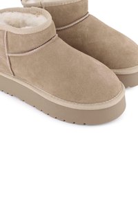 Botas de tobillo de ante marrón claro con un forro suave, punta redondeada y una suela gruesa y texturizada de color beige con pequeños tacos para mayor tracción.