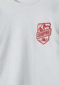 Balts audums ar nelielu sarkanu kempinga emblēmu, uz kuras attēloti kalni, putni, koki un telts, ar vārdu "KEMPINGS" centrā.