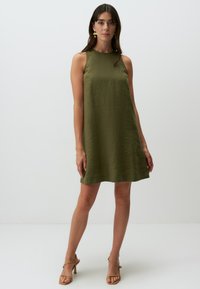 Ärmelloses, olivgrünes Kleid aus strukturiertem Stoff, A-Linie, knielang, mit Rundhalsausschnitt. Tragen mit hellen Sandalen.