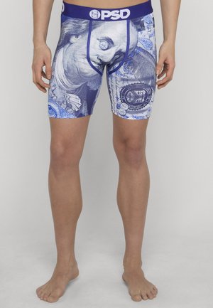 Uomo che indossa boxer con una stampa blu e bianca raffigurante il volto stilizzato di Benjamin Franklin e elementi di valuta su uno sfondo semplice.