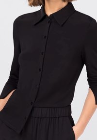 Zwarte button-up shirt gemaakt van een gladde stof, met een kraag, lange mouwen met openingen en een relaxte pasvorm bij de taille.