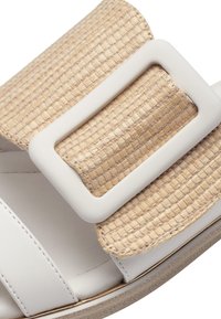 White slide sandal featuring a wide woven straw strap with a large white buckle. Smooth surface and a subtle texture in the strap.