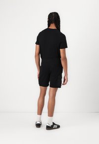 T-shirt noir et shorts cargo, tous deux de couleurs unies. Les shorts cargo comportent des poches latérales. Chaussures noires avec trois rayures blanches et chaussettes blanches.