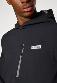 Black hooded jacket with a zippered chest pocket, gray accents, and a Columbia logo patch. Features a smooth fabric texture and minimalistic design.